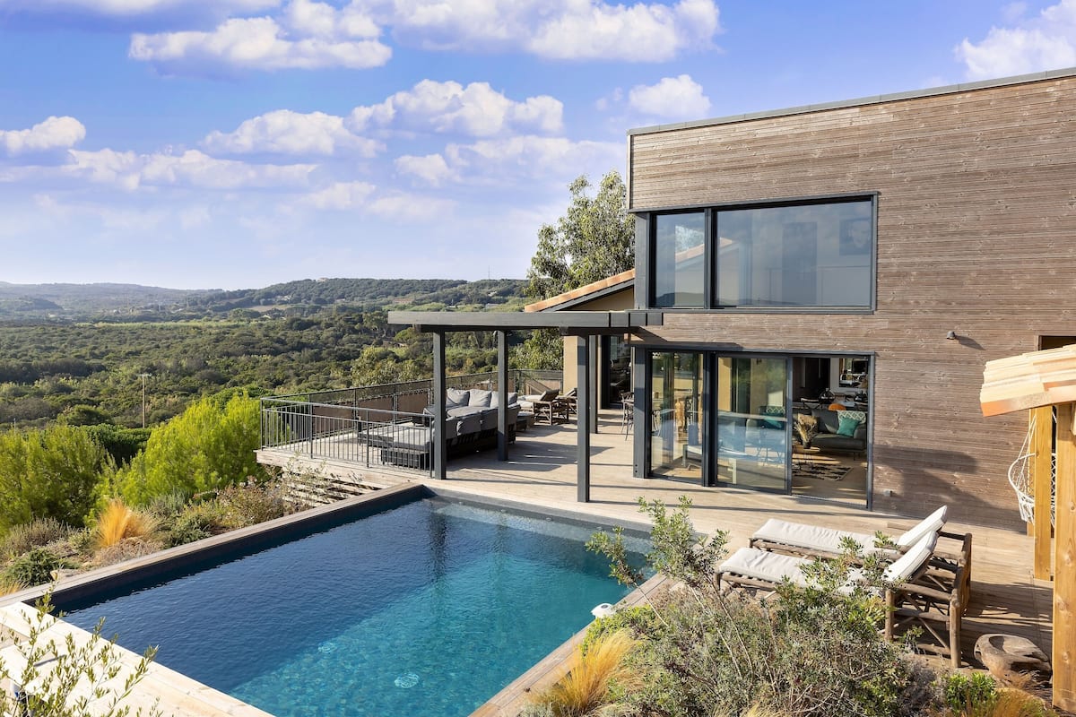 A modern house with a swimming pool, outdoor seating, and a view of the countryside.