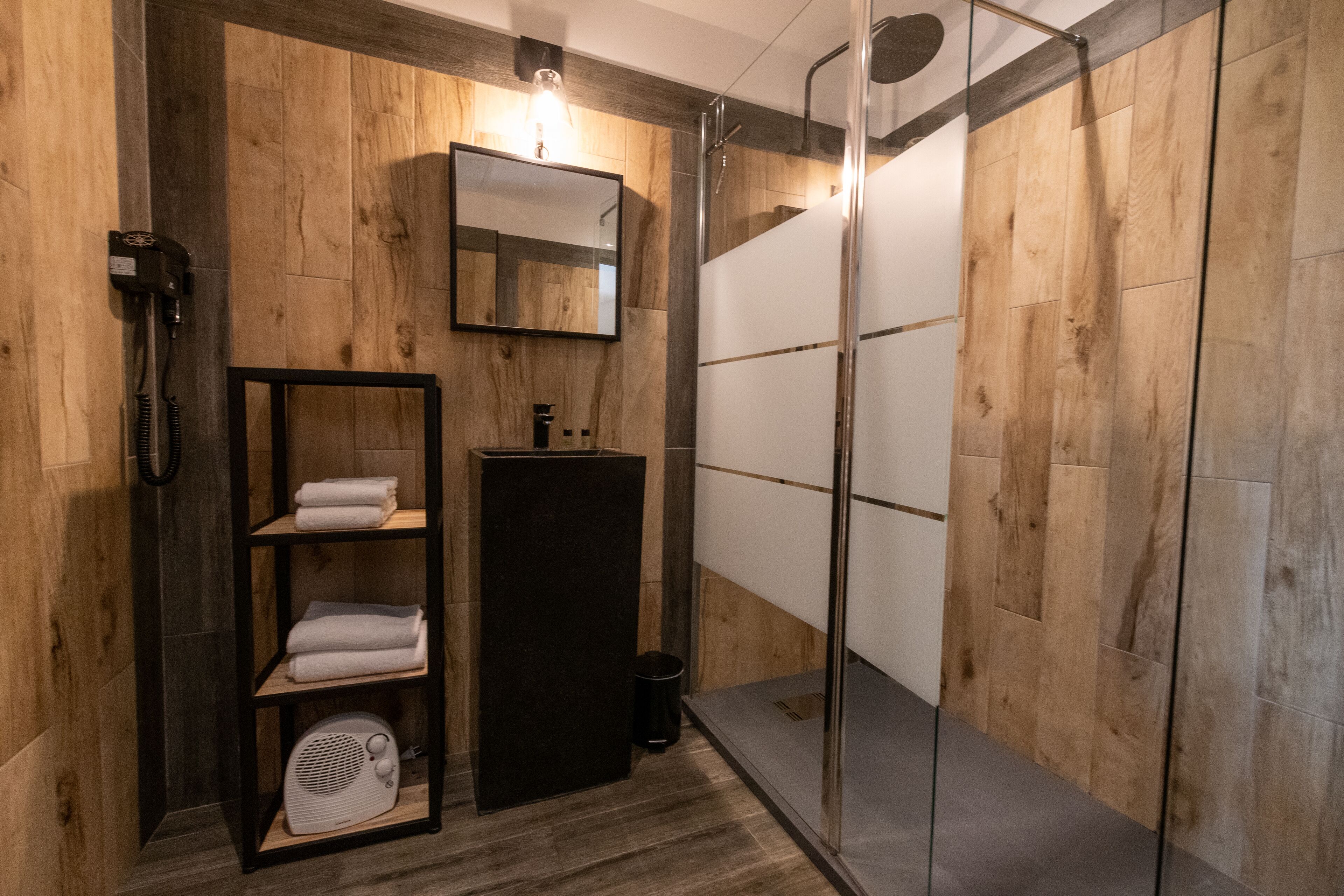 A modern bathroom with a wooden wall design, a glass shower enclosure, and a built-in shelf with towels.