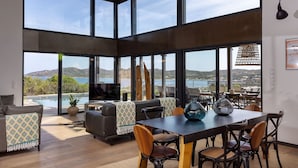 A spacious living area with a large dining table, comfortable seating, and a view of a pool and mountains. - Résidence Casarina (Bonifacio)