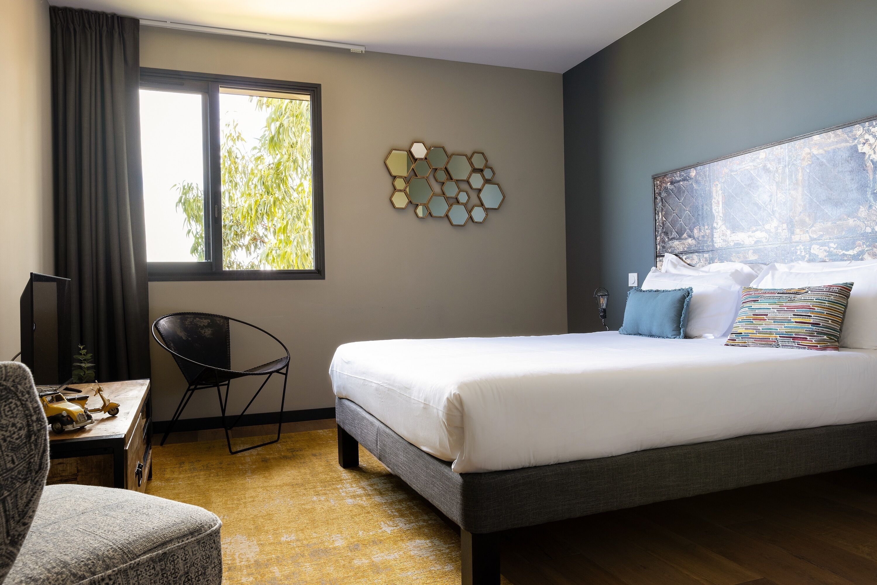 A neatly arranged hotel room with a bed, a chair, a desk, and a large window.
