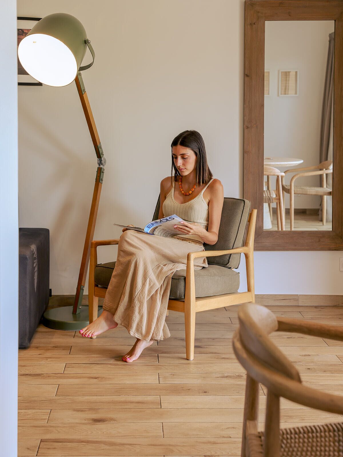 Une pièce avec un plancher en bois, une chaise, un lampadaire et un miroir au mur.