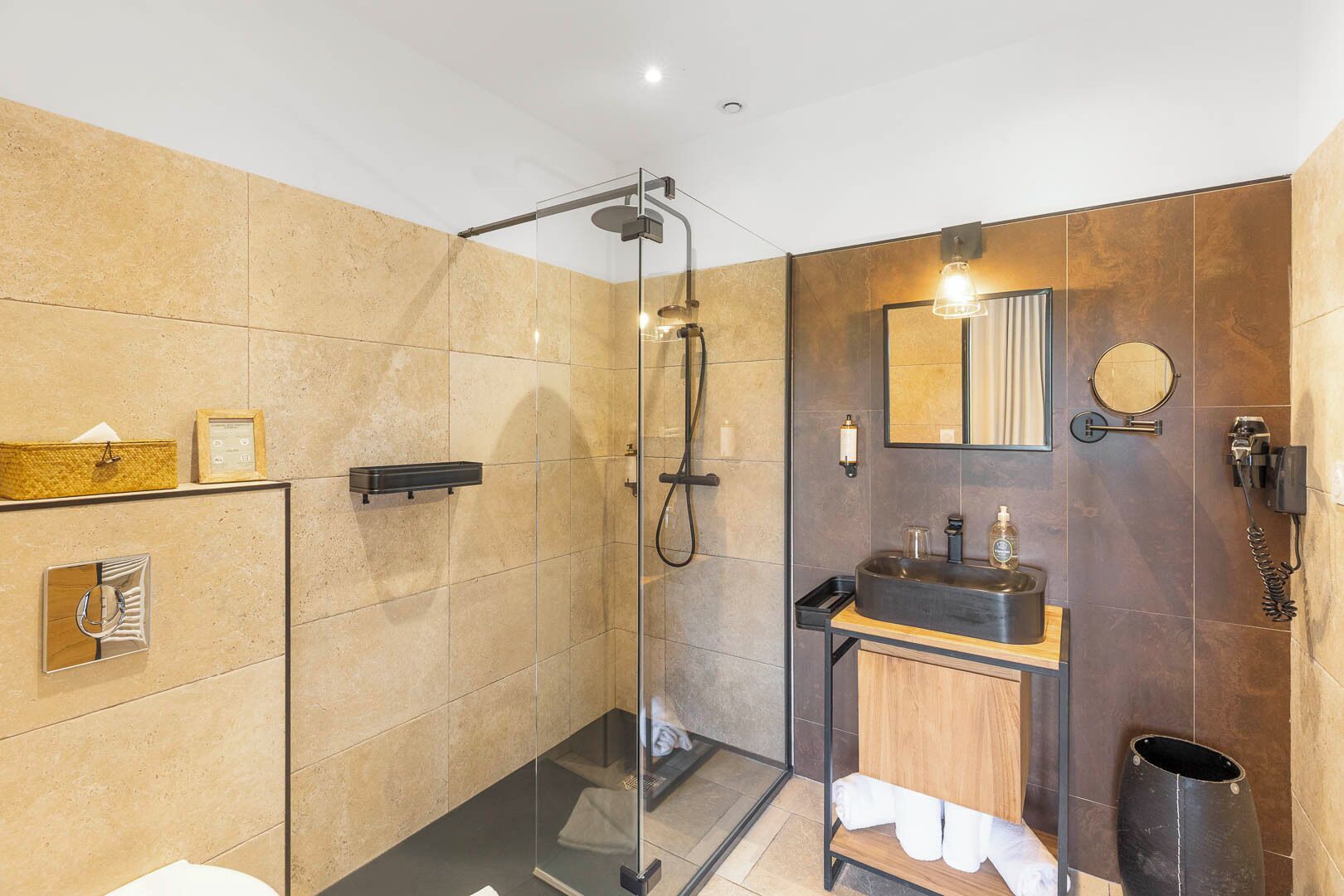 A modern bathroom with a glass-enclosed shower, a wooden vanity with a black sink, and a mirror above the sink.