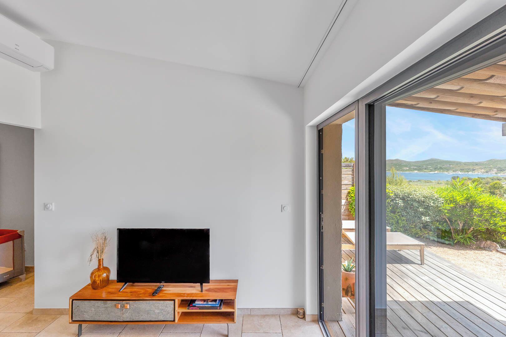 Una sala de estar moderna con un televisor de pantalla plana sobre una consola de madera, y un gran ventanal corredero que da a una terraza con vistas panorámicas.