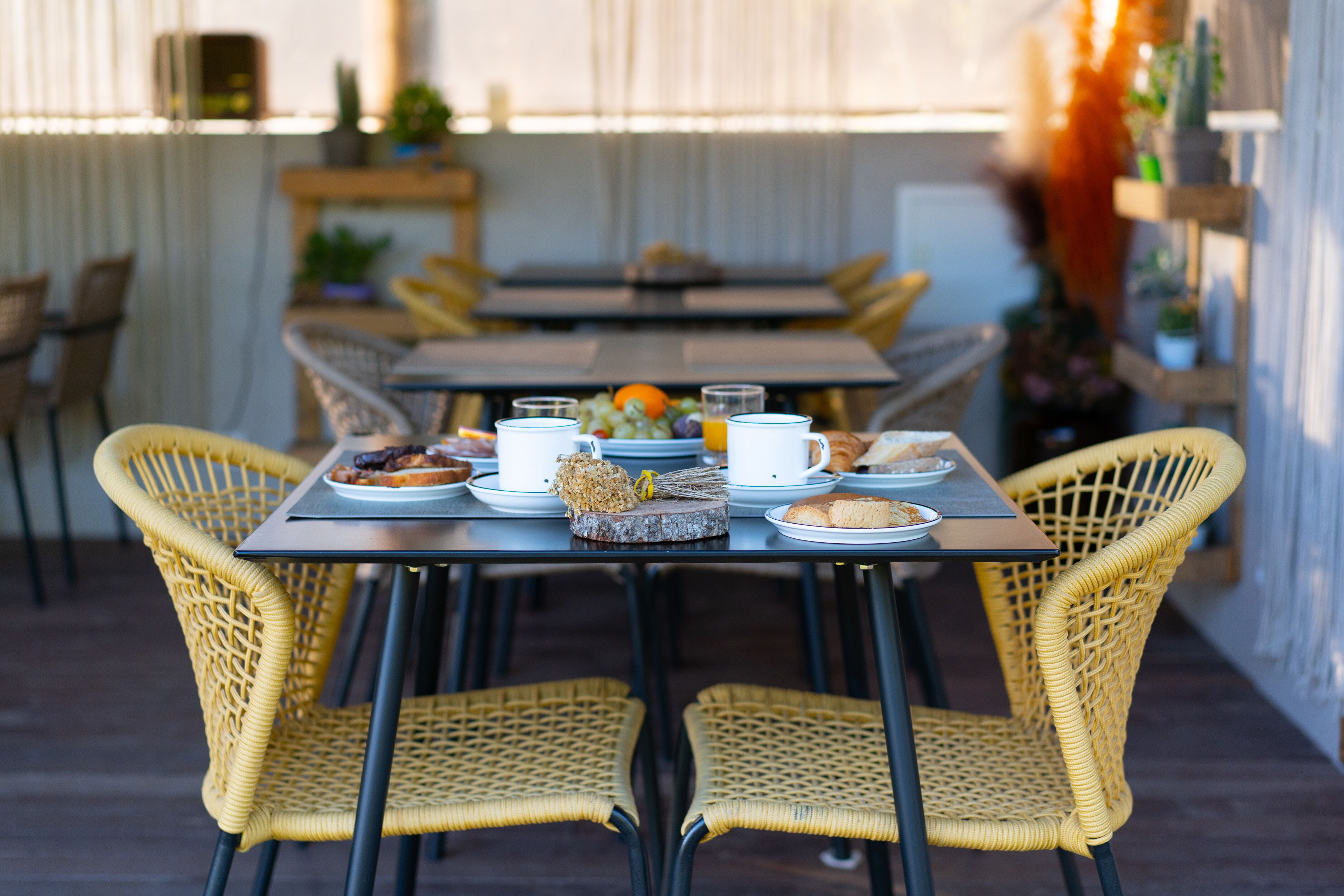 A dining area with wicker chairs and tables, featuring breakfast items like fruit, bread, and coffee.