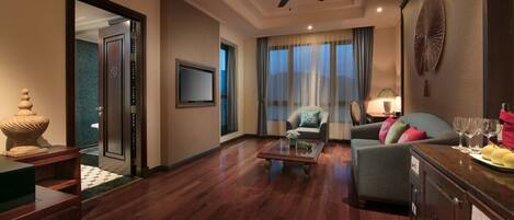 A spacious living room with a wooden floor, a ceiling fan, a sofa, a coffee table, and a TV mounted on the wall.