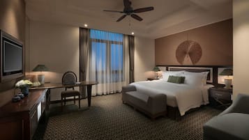 Ein Hotelzimmer mit einem großen Bett, einem Schreibtisch, einem Sessel, einem Fernseher und einem Deckenventilator.
