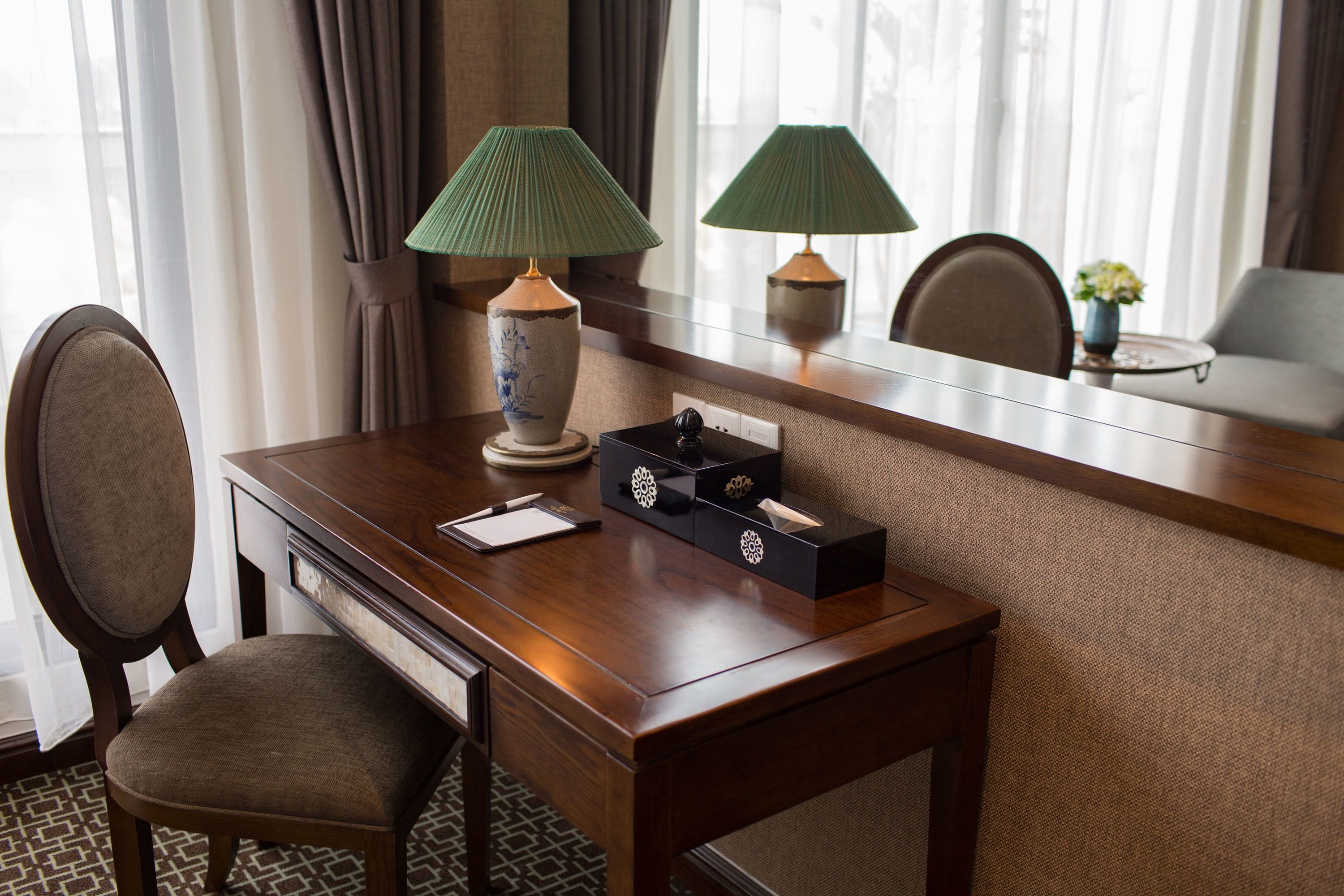 Una camera d'albergo con una scrivania in legno, due lampade, un vaso con fiori e una sedia.