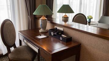Una camera d'albergo con una scrivania in legno, due lampade, un vaso con fiori e una sedia.