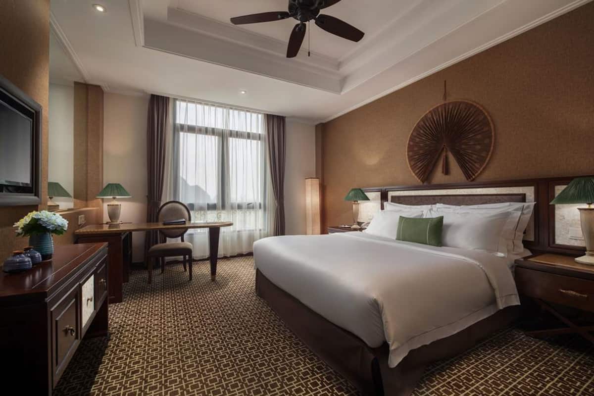 Une chambre d’hôtel avec un grand lit, un bureau, une chaise, une télévision et un ventilateur de plafond.