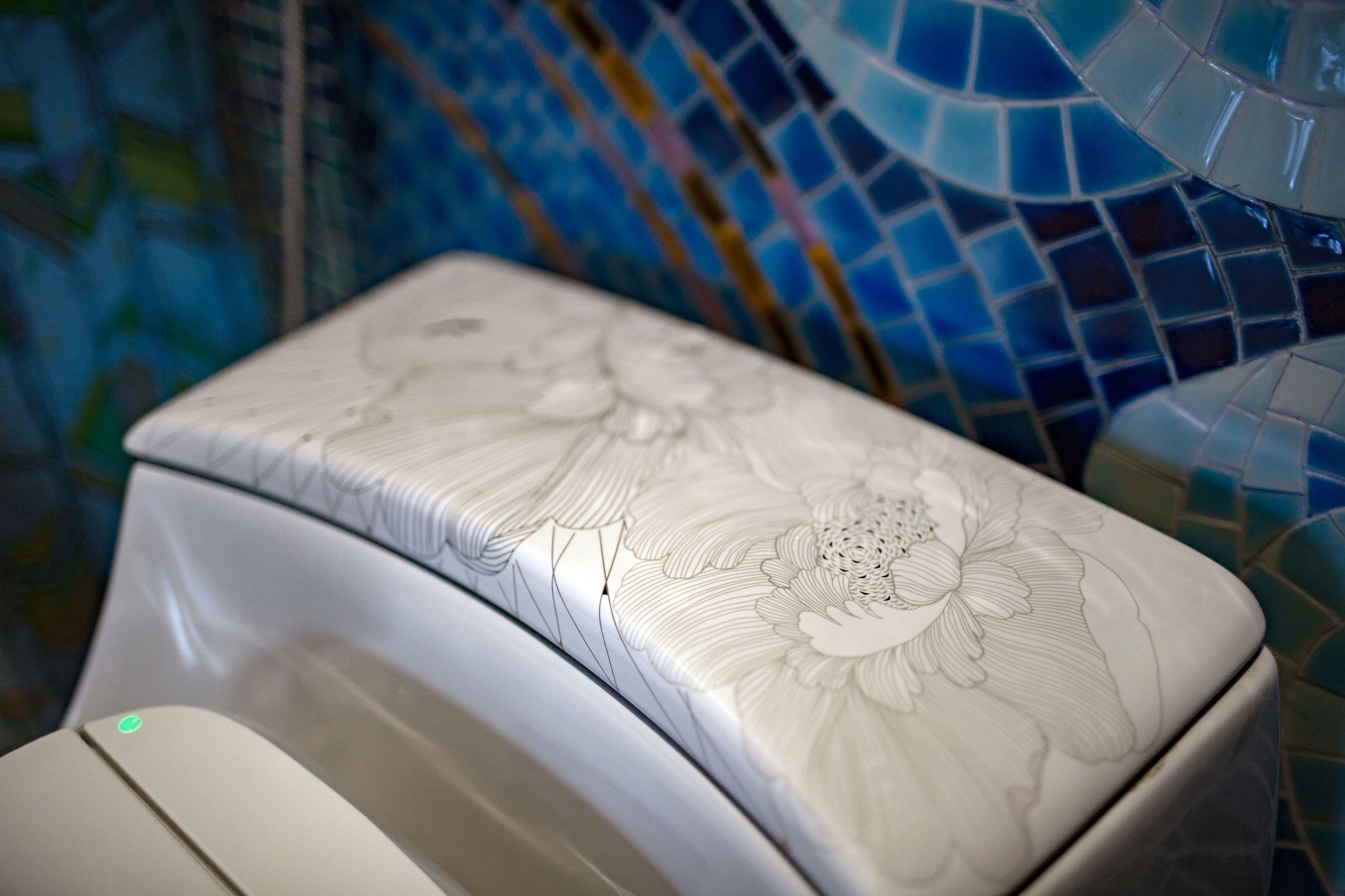 A toilet with a floral design on the lid, set against a mosaic tile wall.