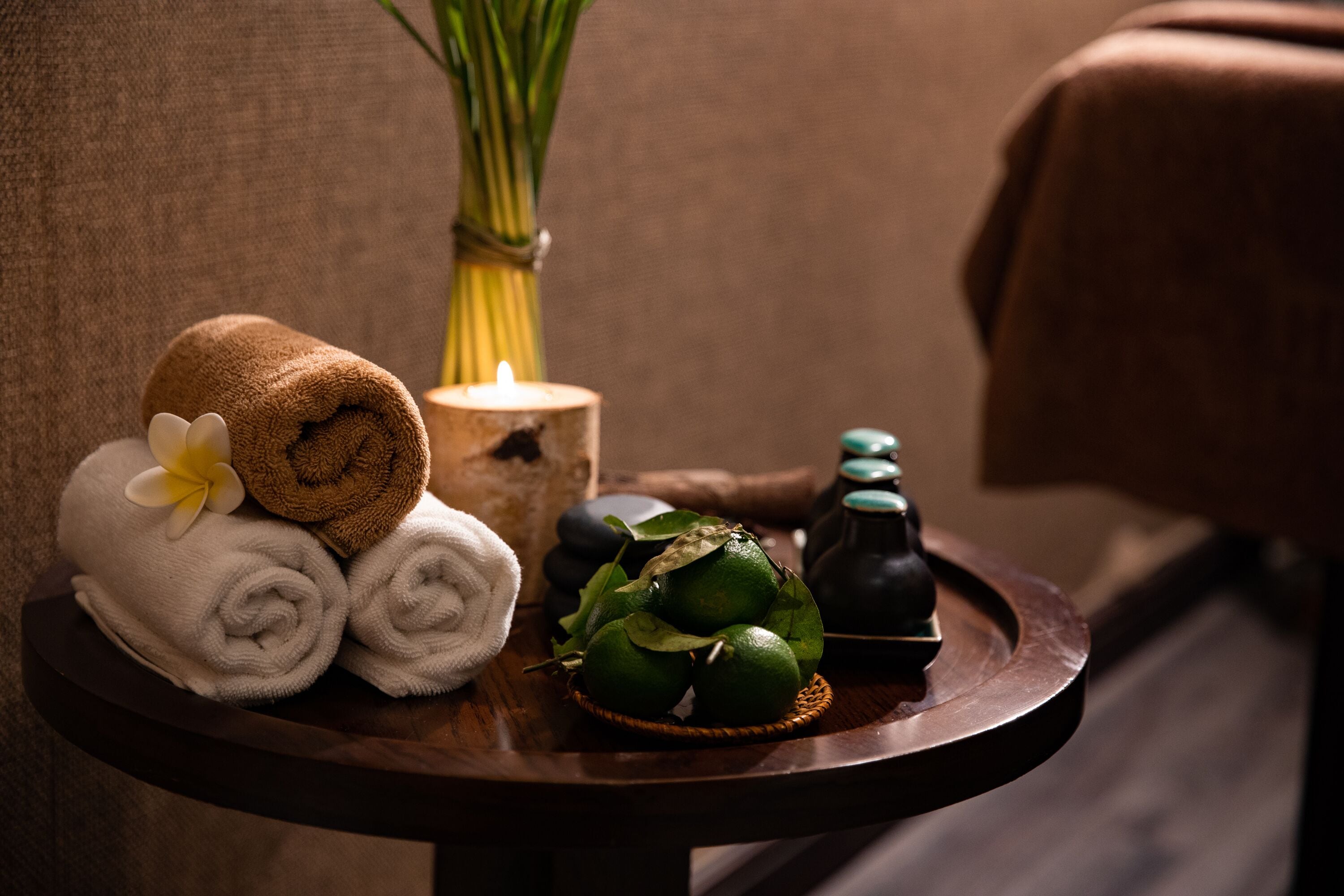 A wooden tray with rolled towels, a lit candle, and fresh green leaves.