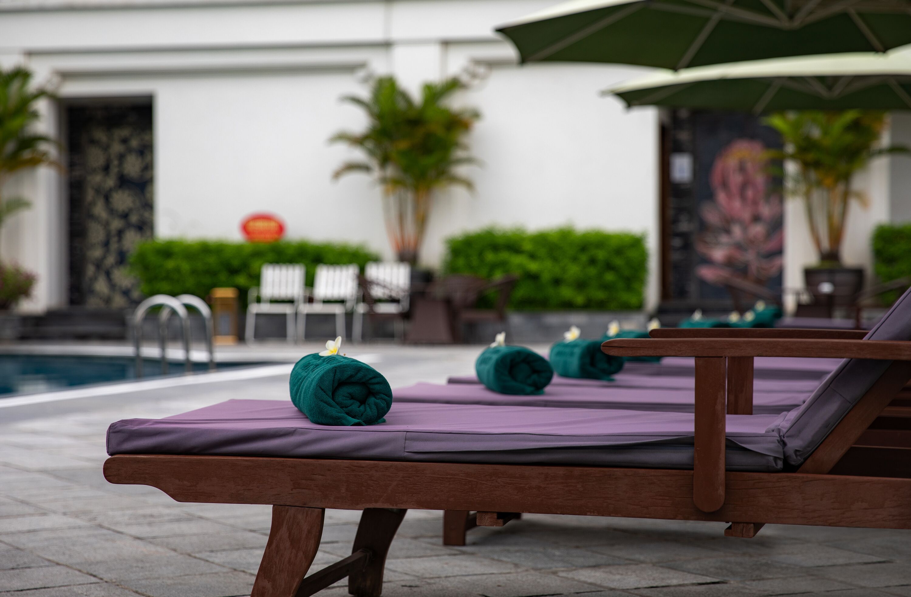 Zona de piscina con sillones de madera y toallas moradas.