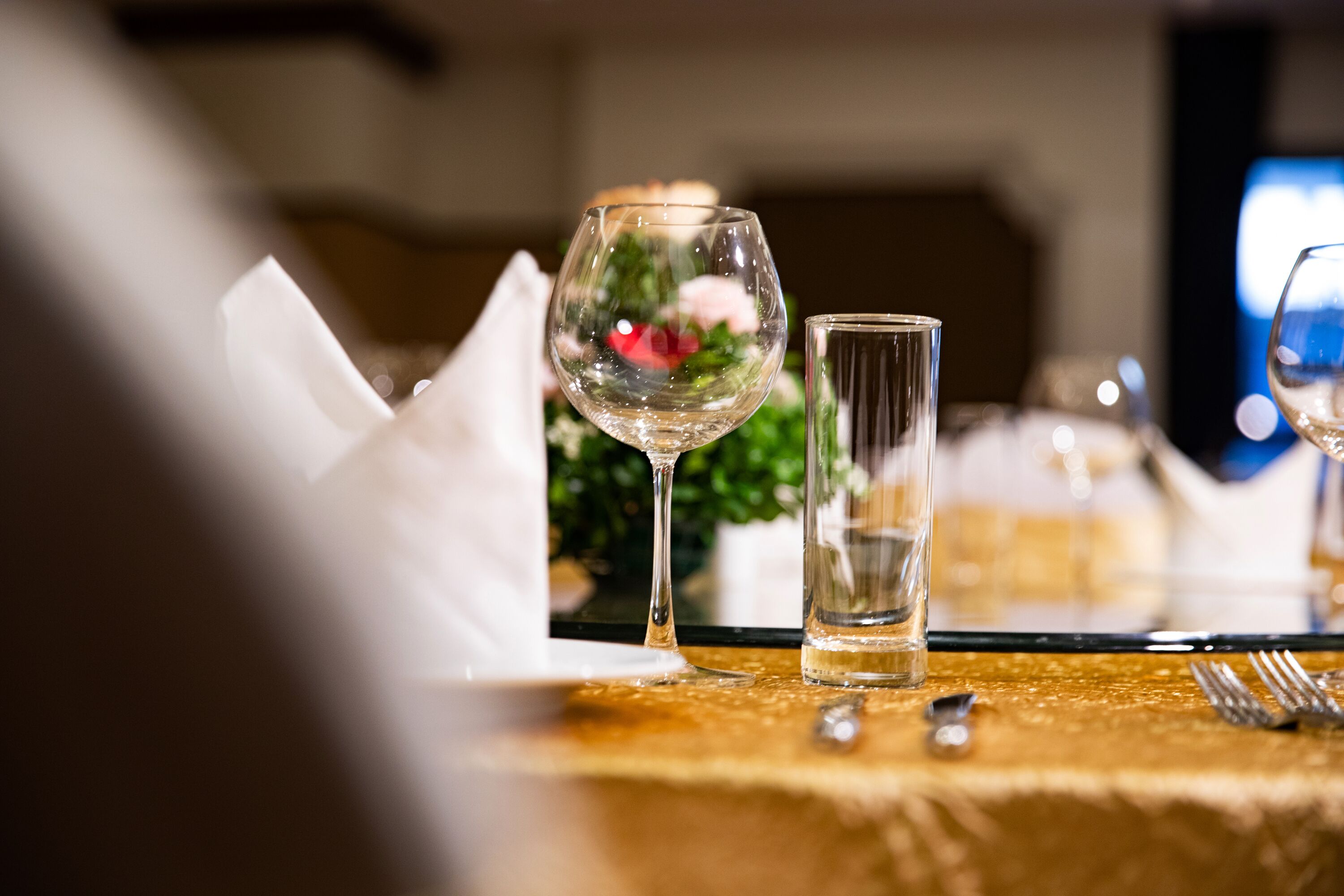 A table set with a gold tablecloth, a wine glass, a water glass, and cutlery.