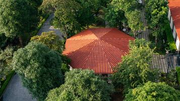 An aerial view of a courtyard with a tiled roof structure surrounded by lush greenery and a paved walkway.