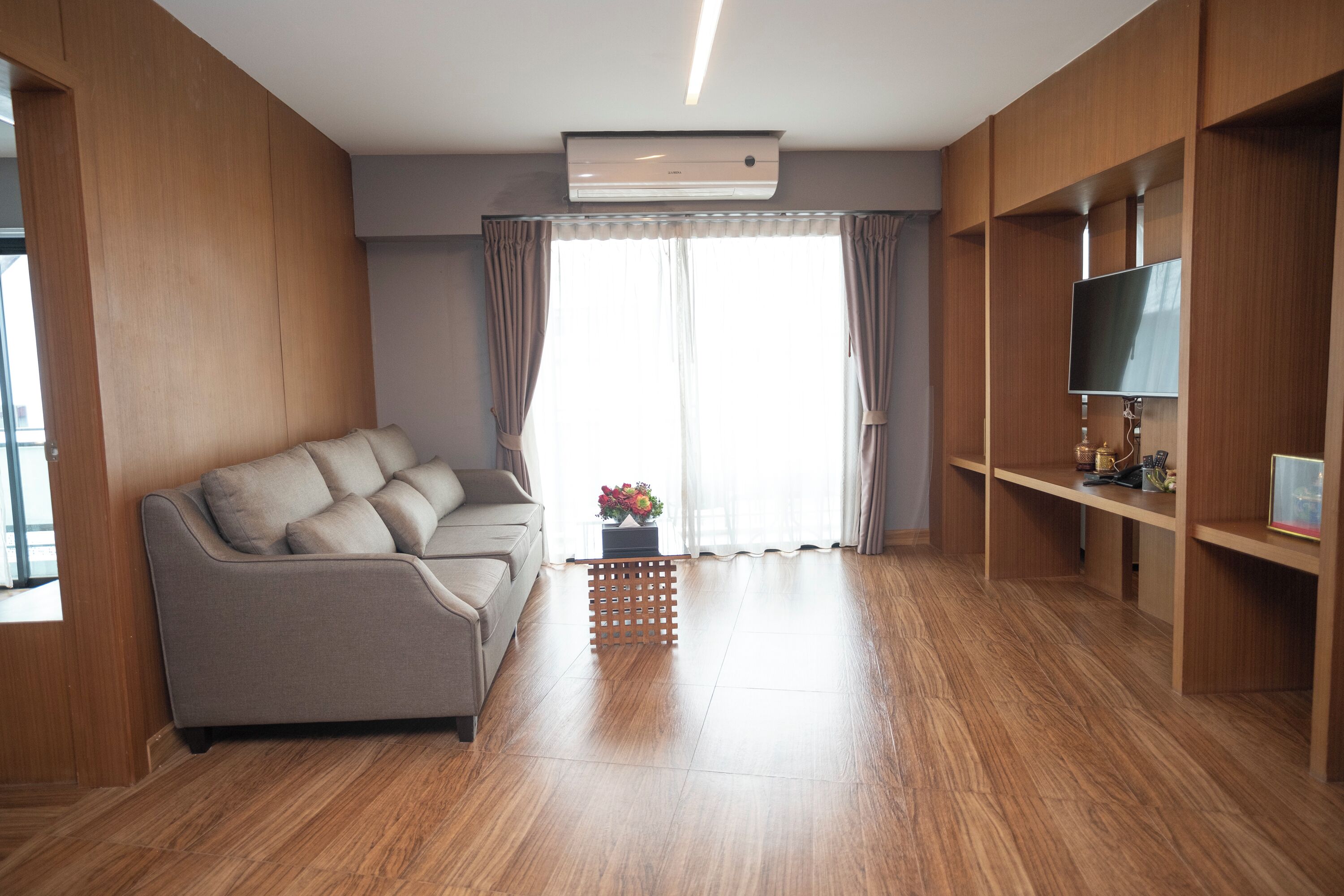 A modern living room with a sofa, wooden flooring, a television, and a large window with curtains.