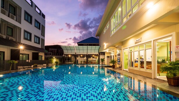 A swimming pool with a tiled floor, surrounded by buildings with large windows and a covered area.
