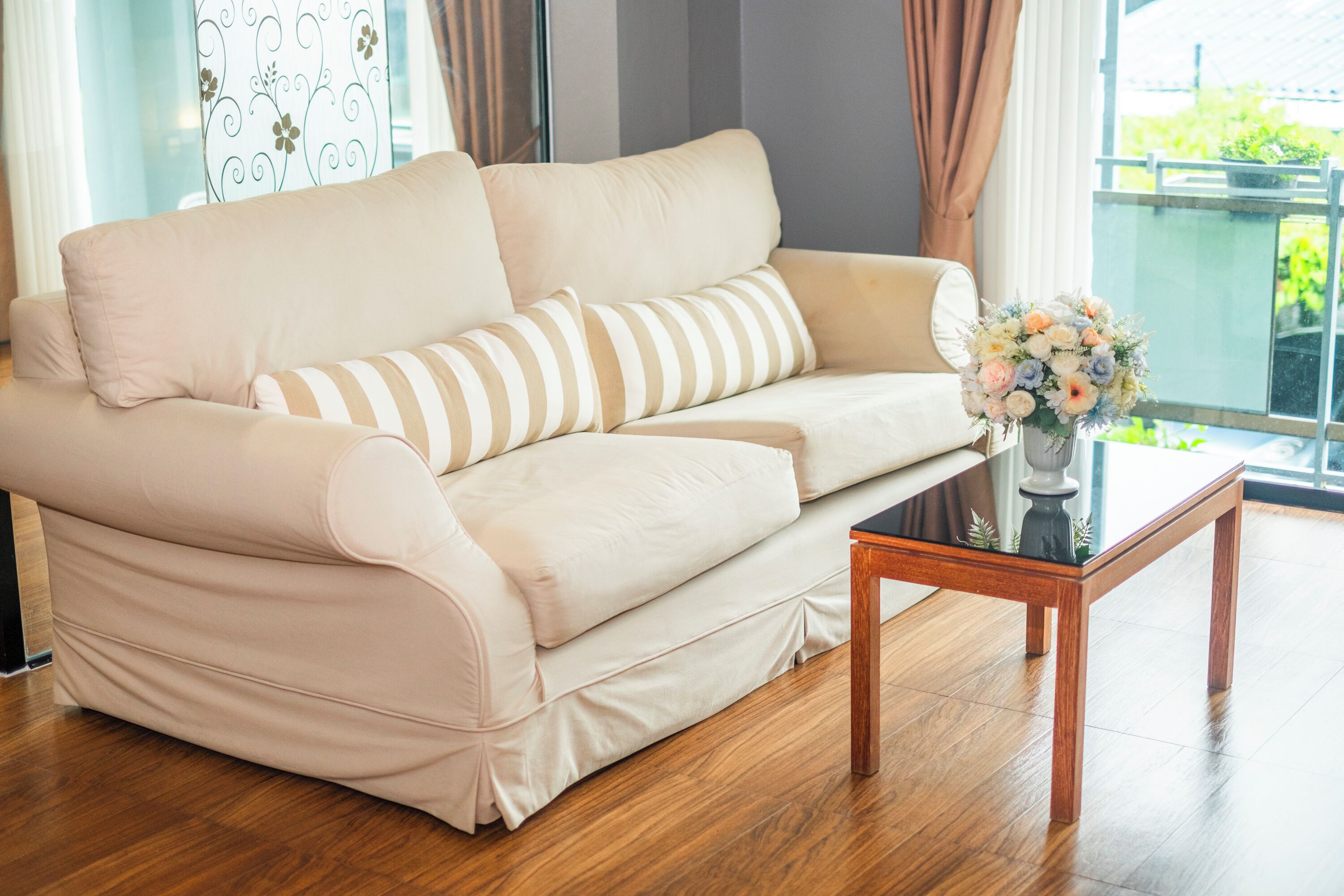 Un sofá beige con almohadones a rayas, una mesa de centro de madera y un florero con flores.