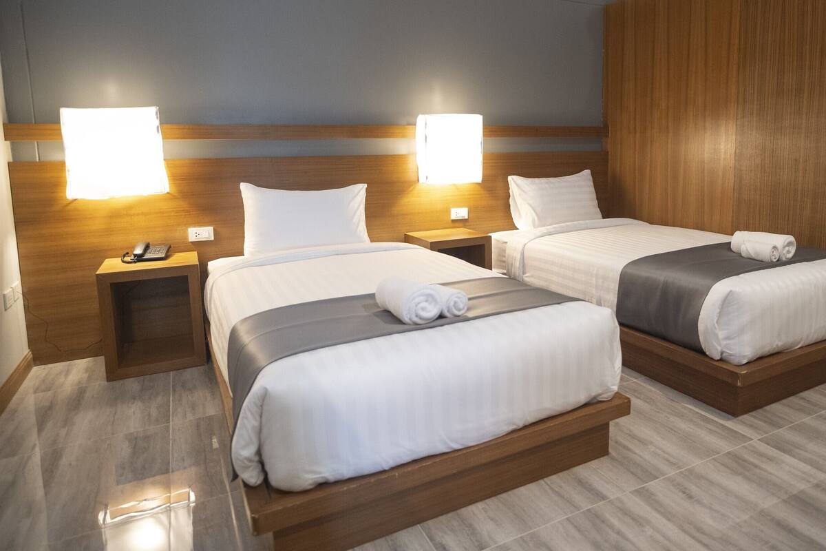 A hotel room with two beds, bedside lamps, a phone on the nightstand, and a wooden headboard.