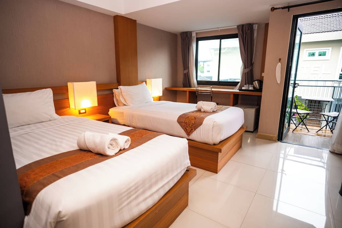 A hotel room with two beds, a desk, a chair, a window with curtains, and a balcony.