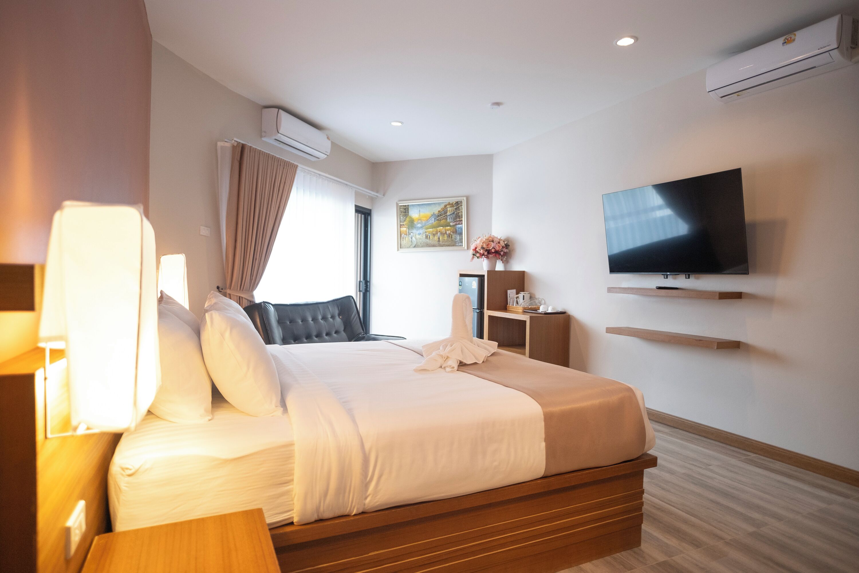 Una habitación de hotel moderna con cama, mesita de noche, televisor, aire acondicionado y un cuadro en la pared.
