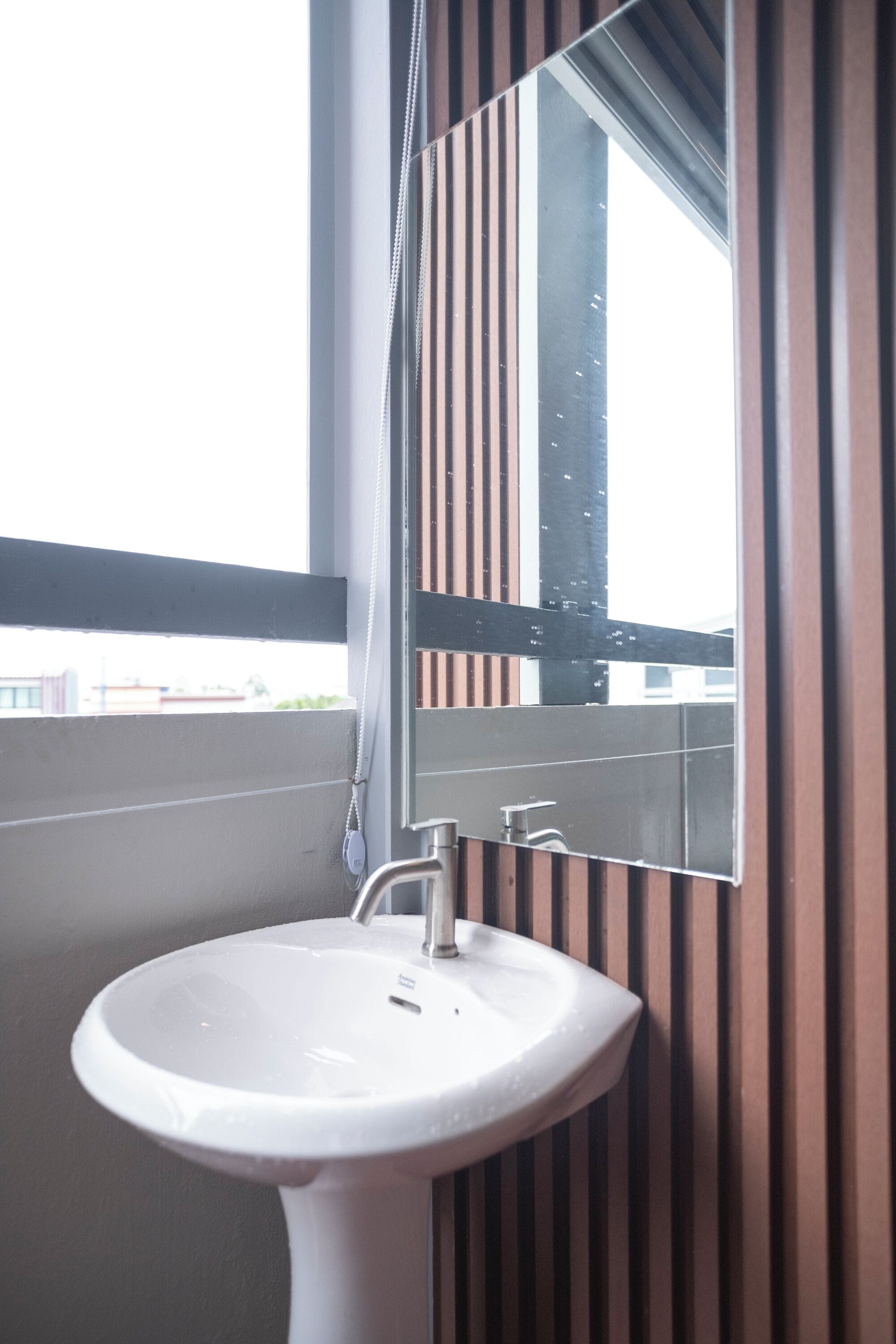 A bathroom with a white sink, a mirror, and a window with a view of buildings.