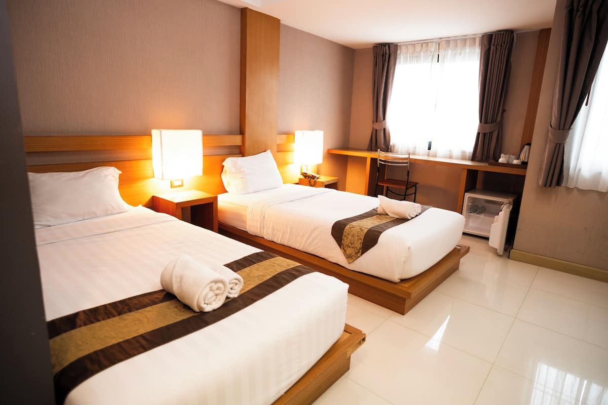 A hotel room with two beds, bedside lamps, a desk, and a chair.