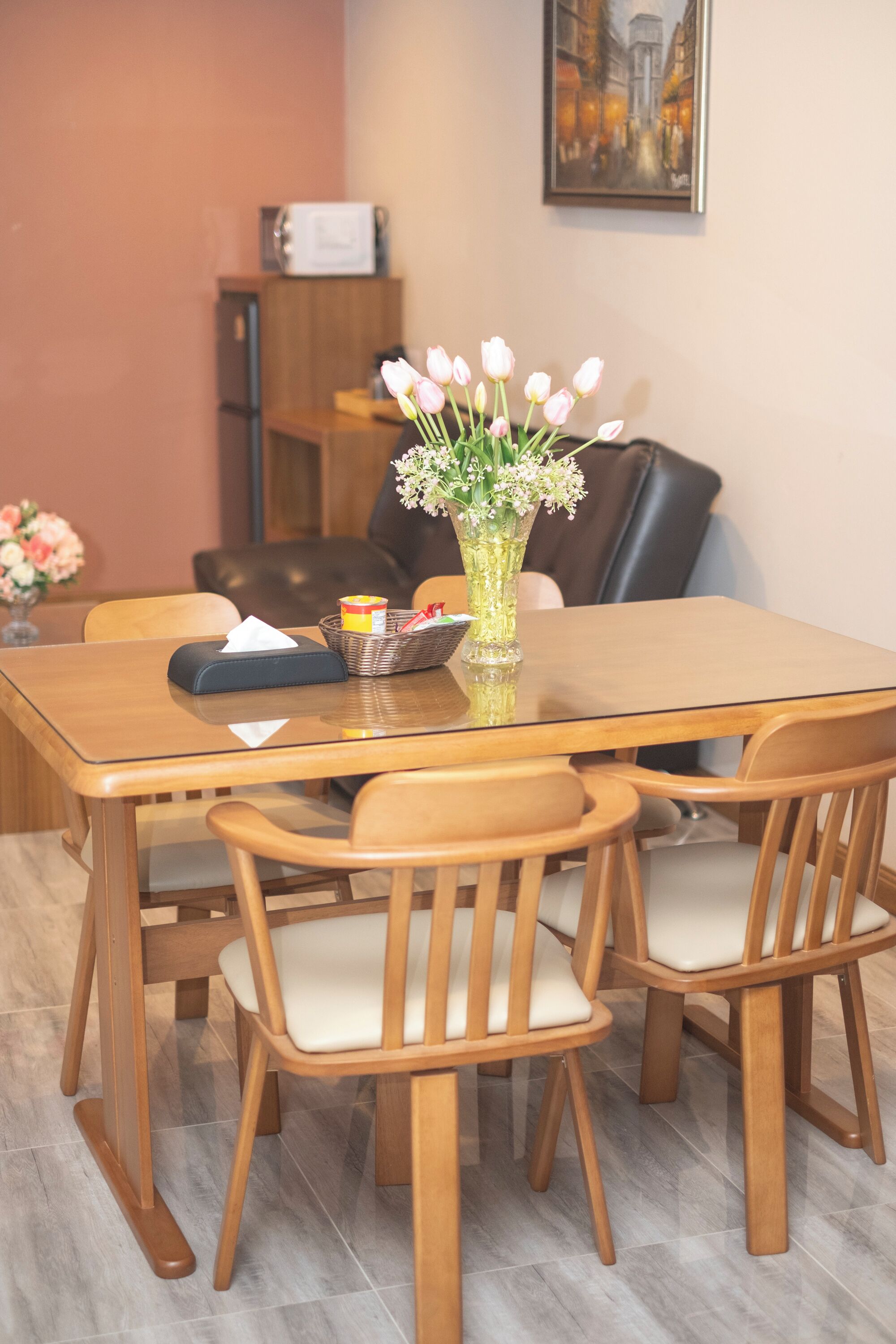Zona pranzo con tavolo in legno, sei sedie, un vaso con fiori, un cesto con oggetti e un quadro appeso al muro.