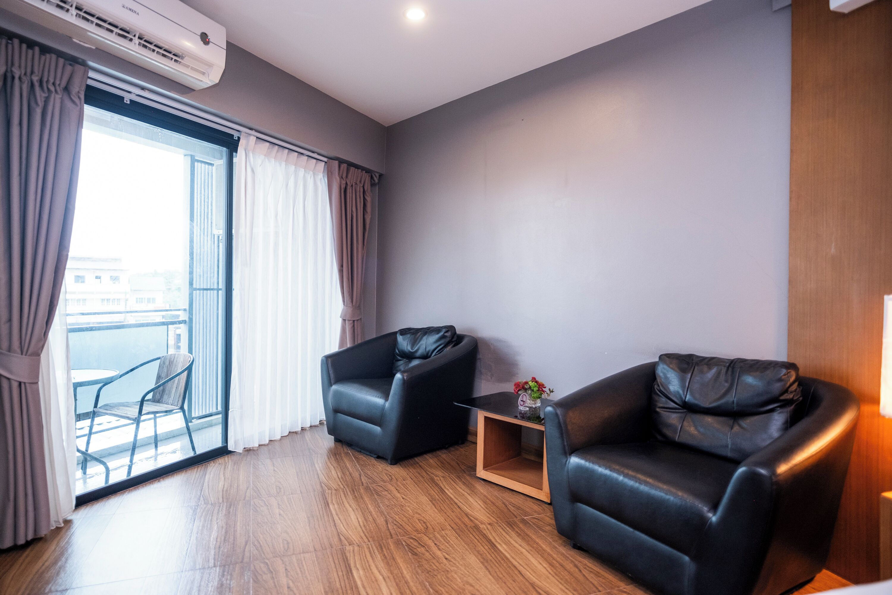 Una sala de estar moderna con dos sillones de cuero, una mesita de madera y un ventanal que da a un balcón.