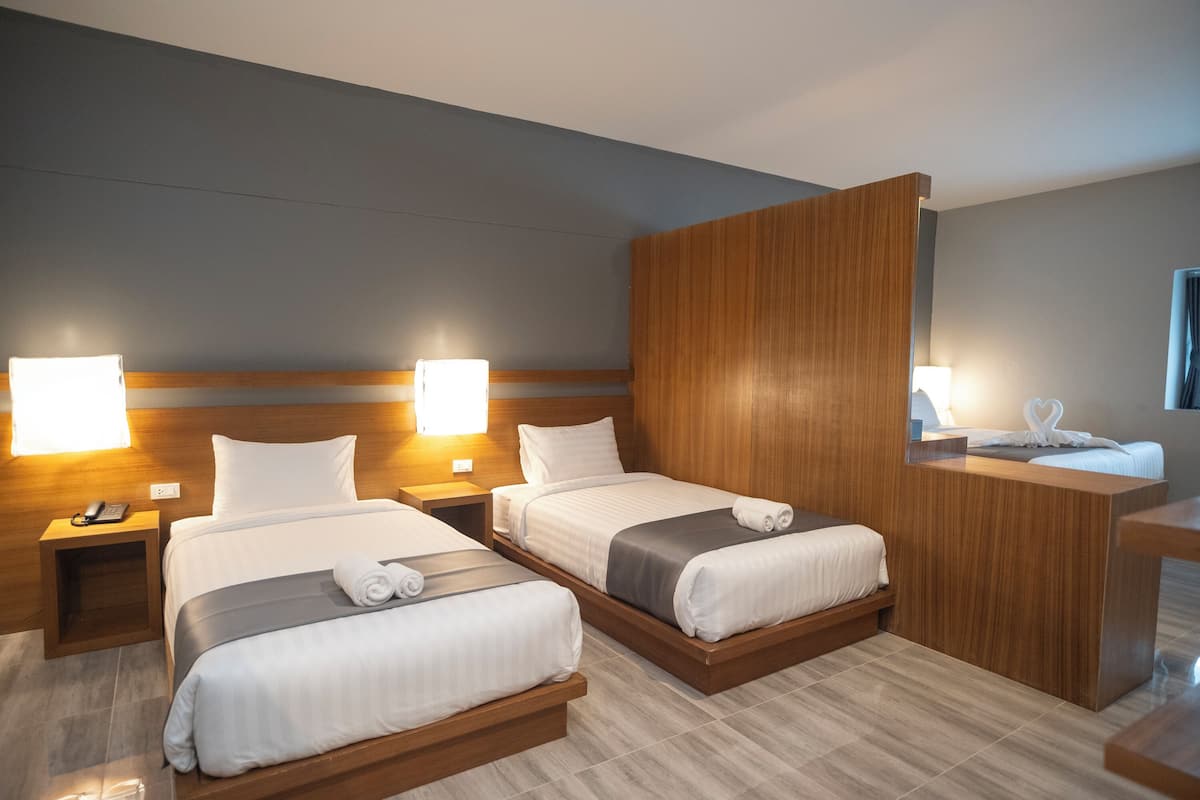 A hotel room with two beds, a wooden headboard, bedside lamps, a desk with a mirror, and a towel rack.