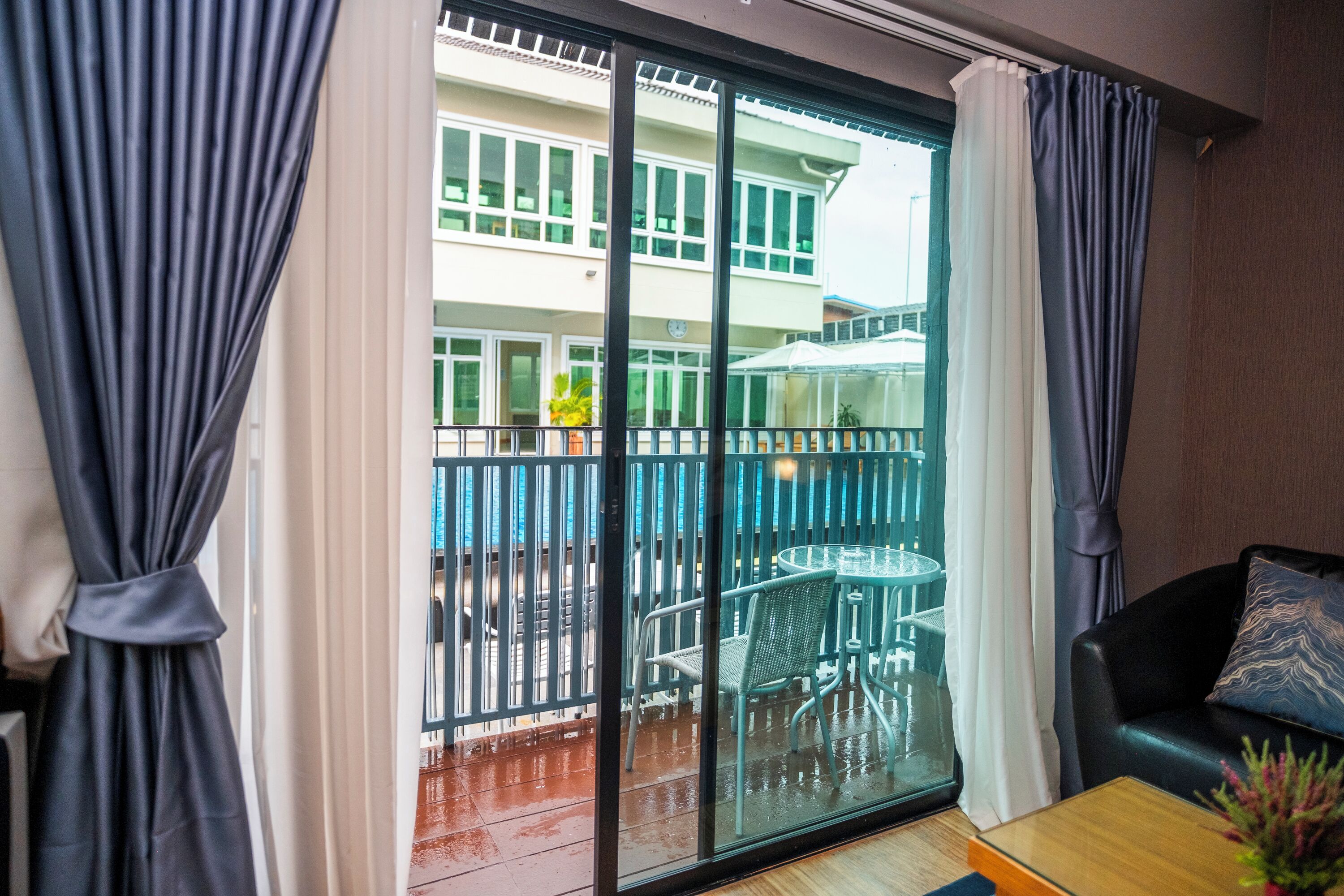 A room with a sliding glass door to an outdoor area, a black leather sofa, and a wooden coffee table.