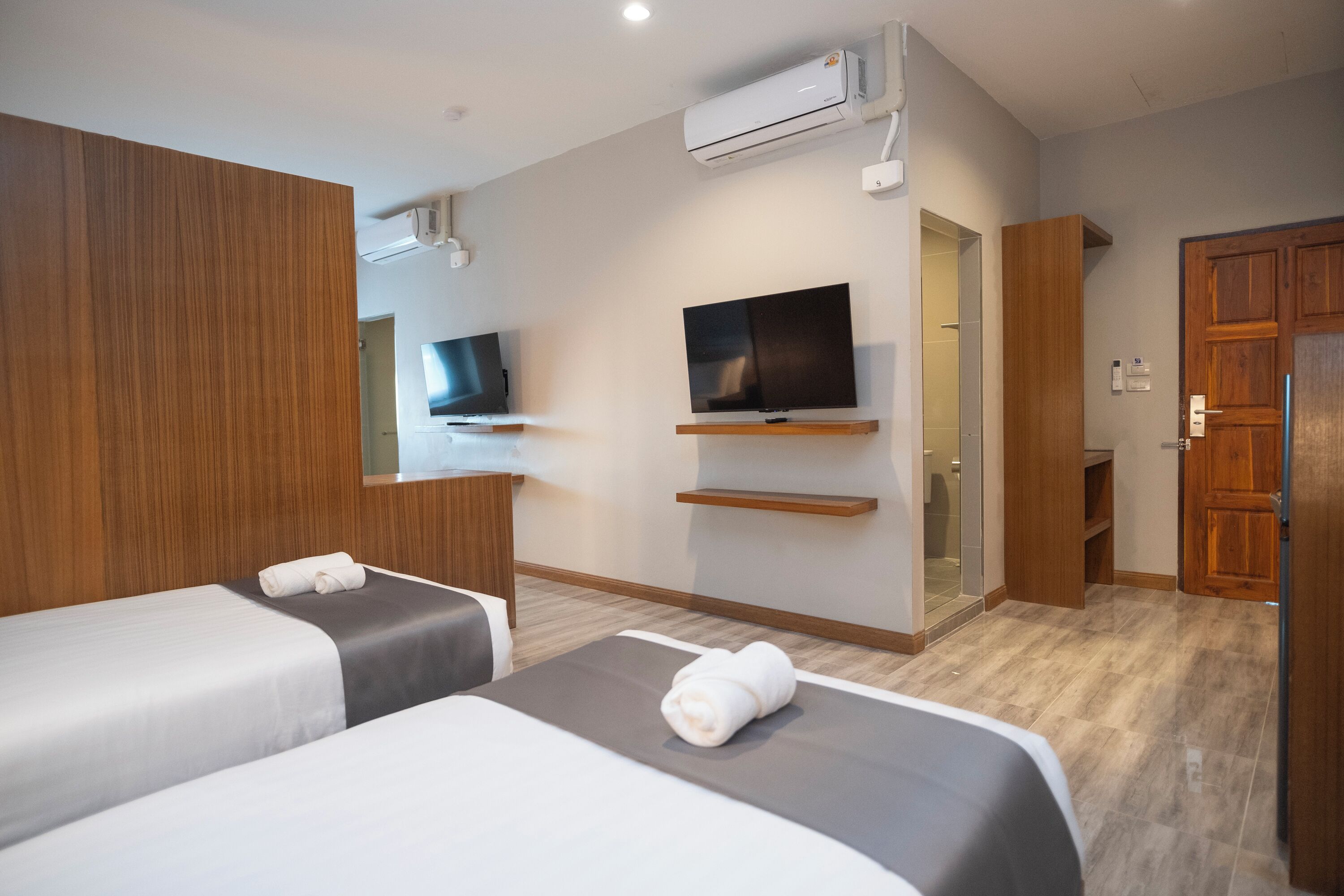 Habitación de hotel con dos camas, televisión, aire acondicionado y armario de madera.