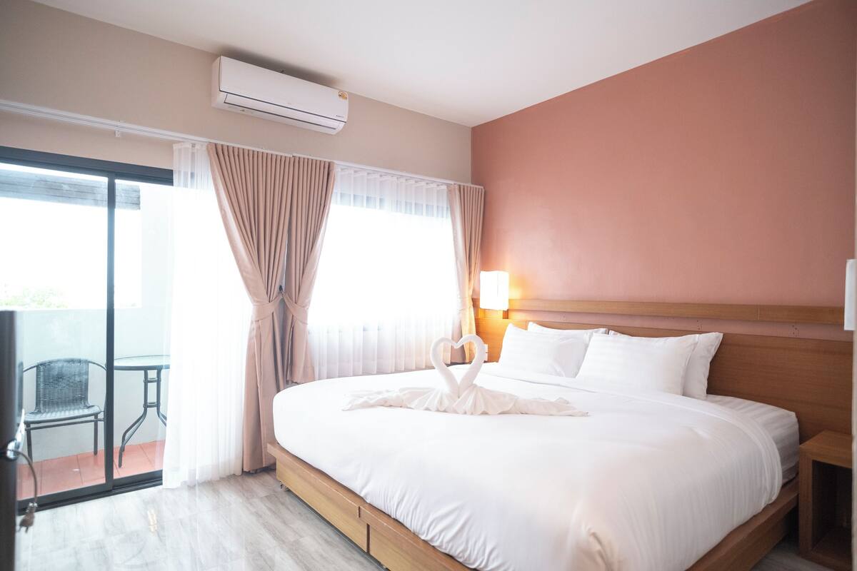 A hotel room with a bed, a nightstand, a lamp, a window with curtains, and a view of the outside.