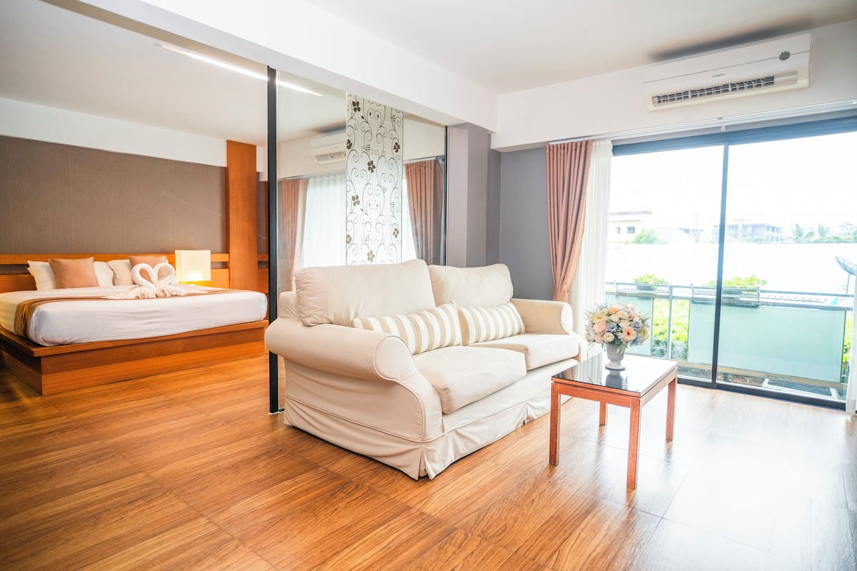 A hotel room with a bed, a sofa, a small table with a vase, and a large window with a view.