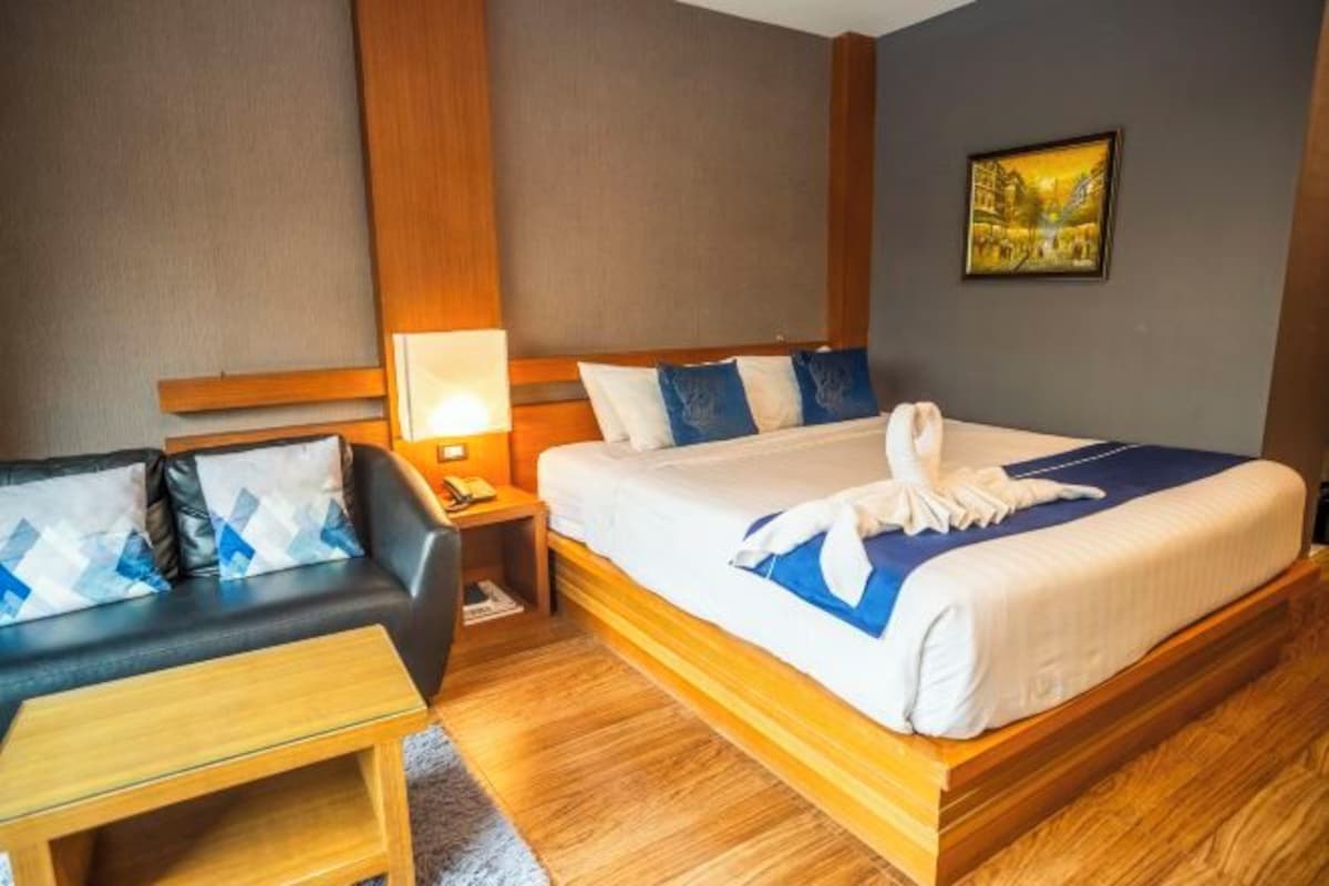 A hotel room with a bed, a sofa, a nightstand, and a painting on the wall.
