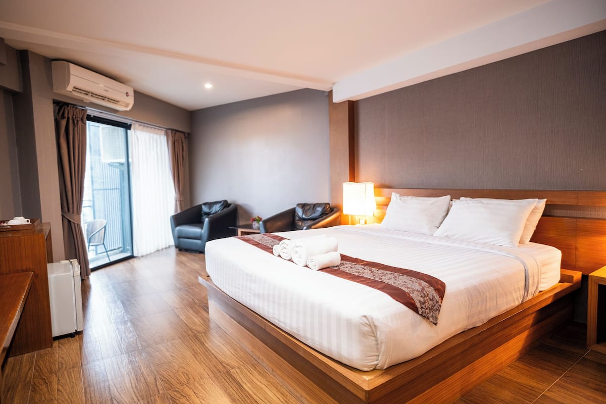 A hotel room with a large bed, a desk, a chair, an air conditioning unit, and a view of the outside.