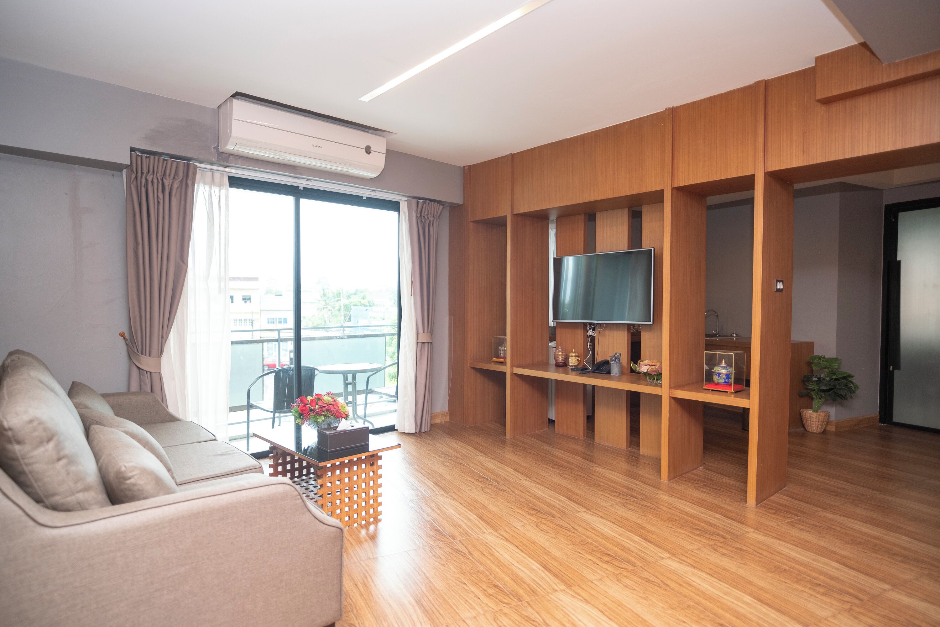 Una sala de estar moderna con un sofá, un televisor en un estante de madera y un balcón con una mesa y sillas.