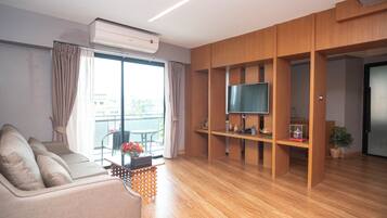 Una sala de estar moderna con un sofá, un televisor en un estante de madera y un balcón con una mesa y sillas.
