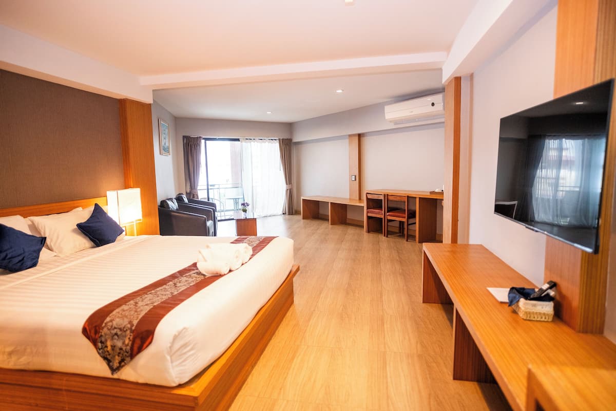A hotel room with a large bed, a desk, a television, and a balcony with a view.