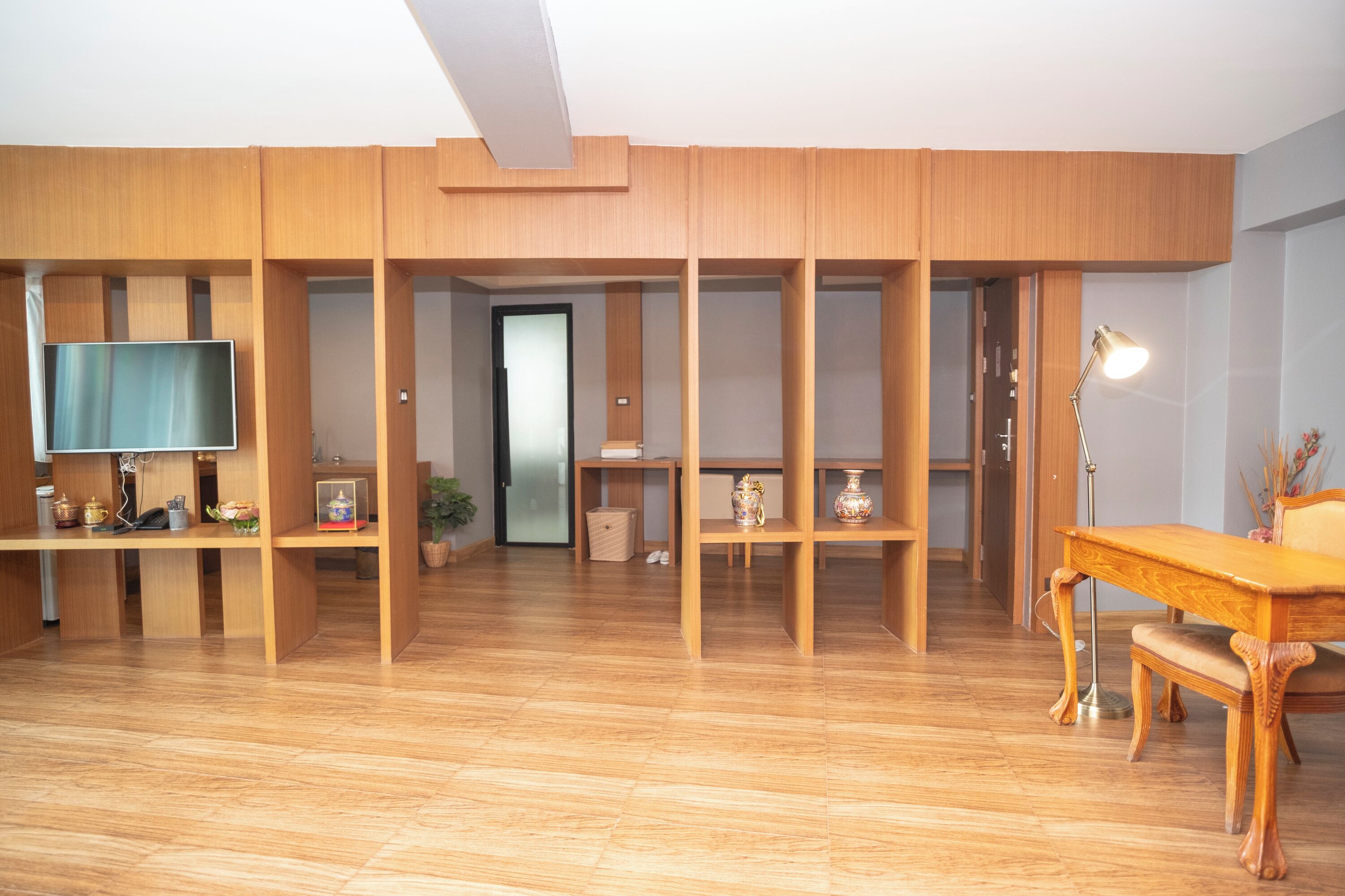 A room with wooden paneling, a television, a desk with a lamp, and a chair.