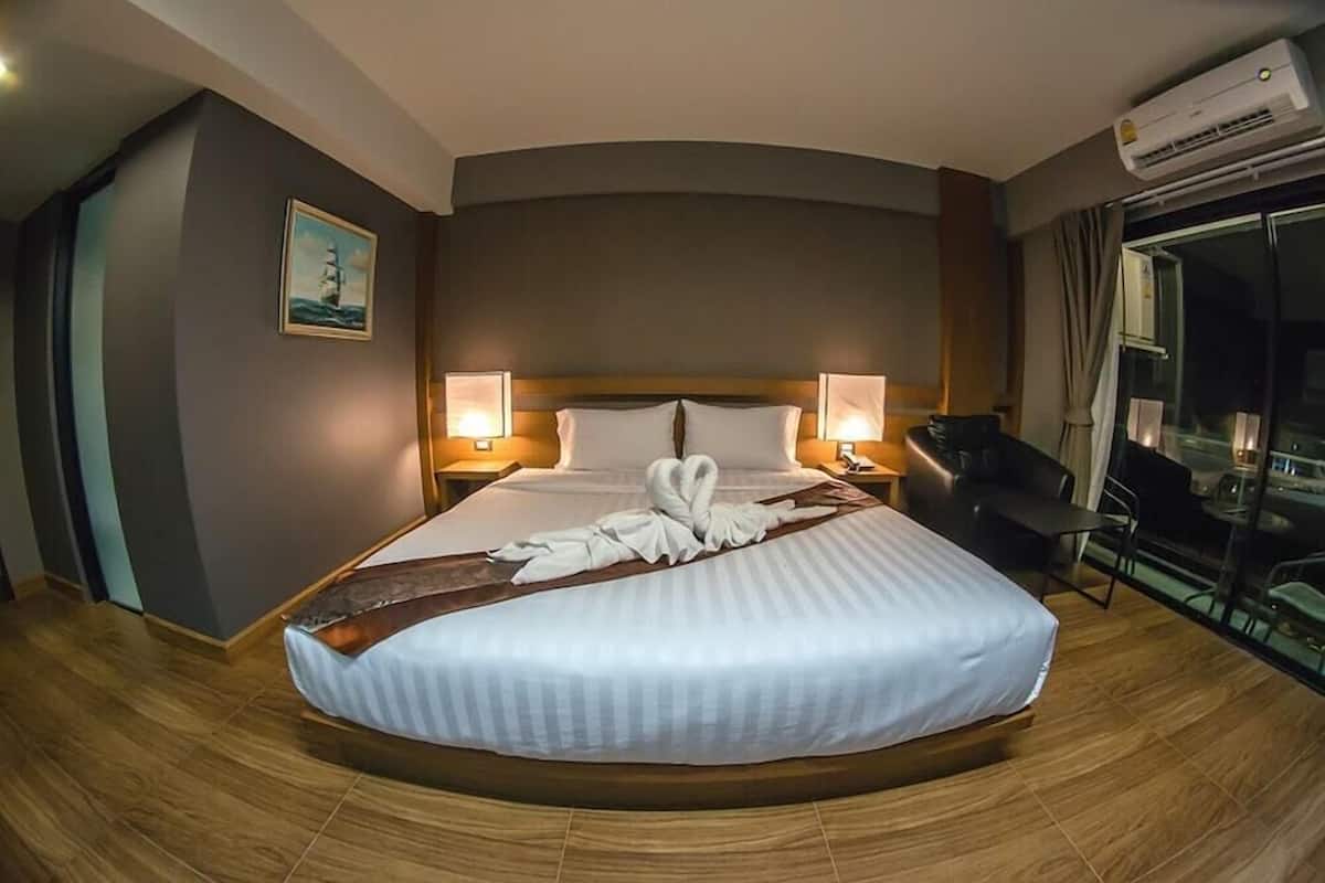 A hotel room with a large bed, two bedside tables with lamps, a painting on the wall, and a view through a glass door.