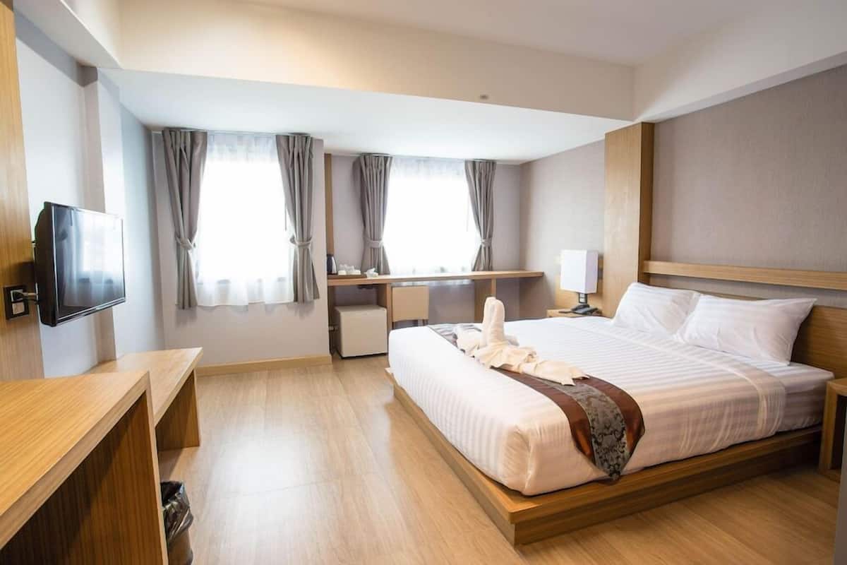 A hotel room with a bed, bedside table, TV, desk, and curtains.