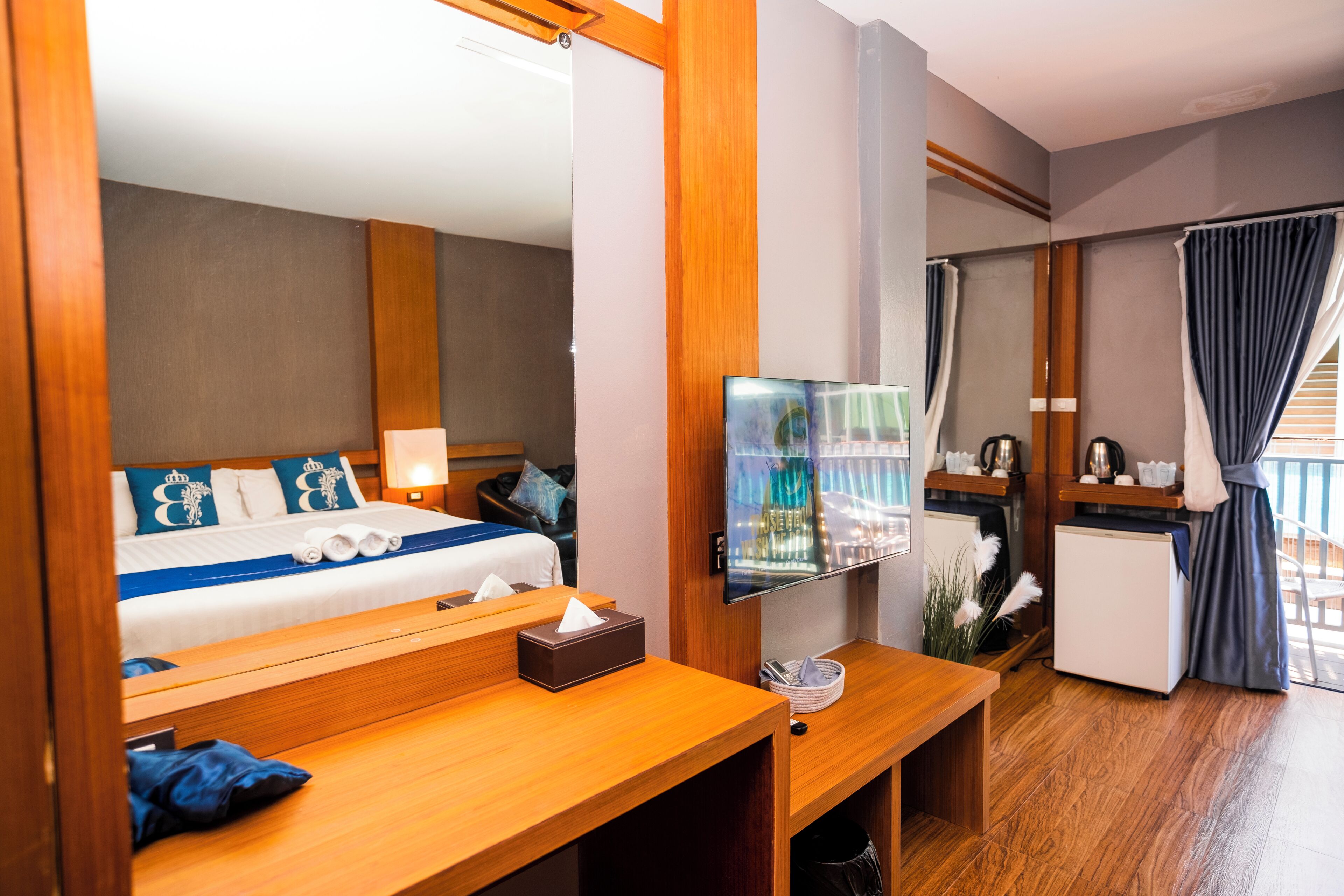 A hotel room with a bed, a TV, a desk, a mini-fridge, and a balcony with curtains.