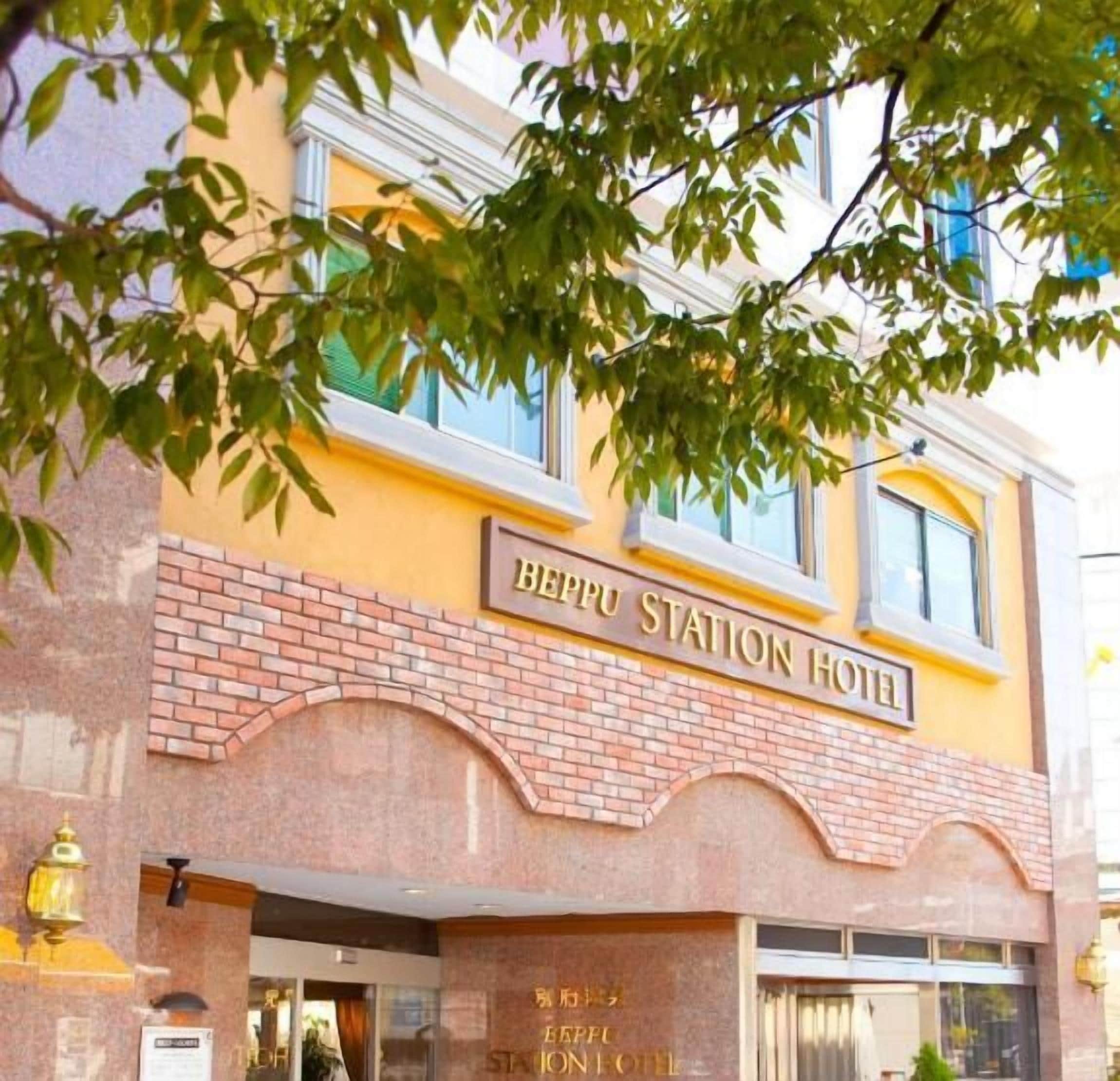 A hotel with a yellow facade, a brick entrance, and a sign that reads "Beppu Station Hotel".