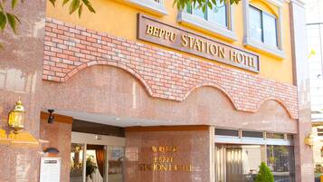 The exterior of the Bepu Station Hotel with a brick facade, large windows, and a potted plant outside.
