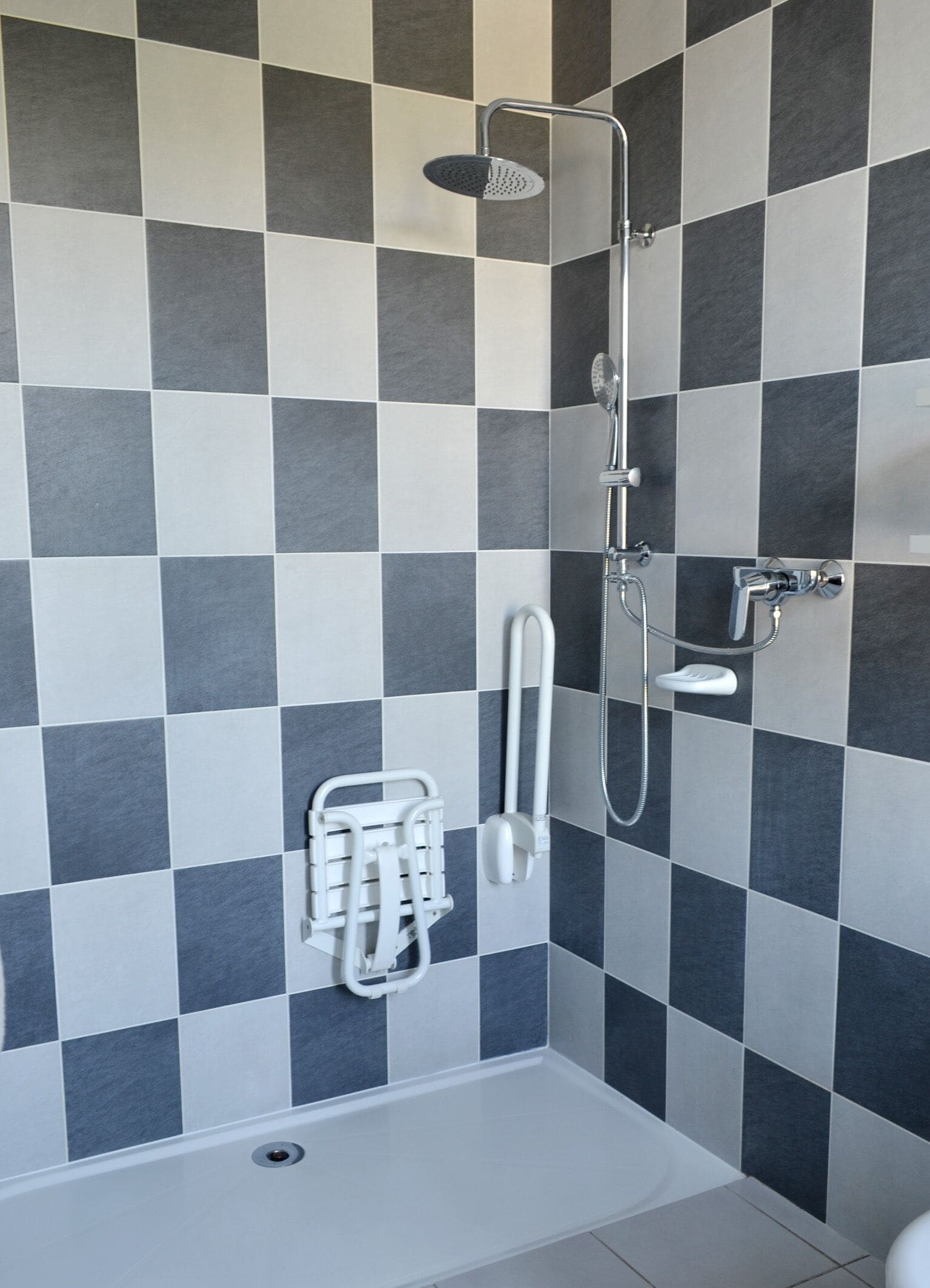Un espace douche avec un mur recouvert de carreaux à motifs à carreaux, une douchette à main, un robinet mural et une autre douchette à main.