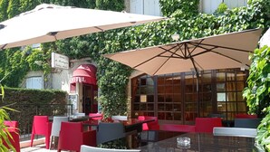 An outdoor seating area with tables and chairs, a large umbrella, and a hotel entrance.