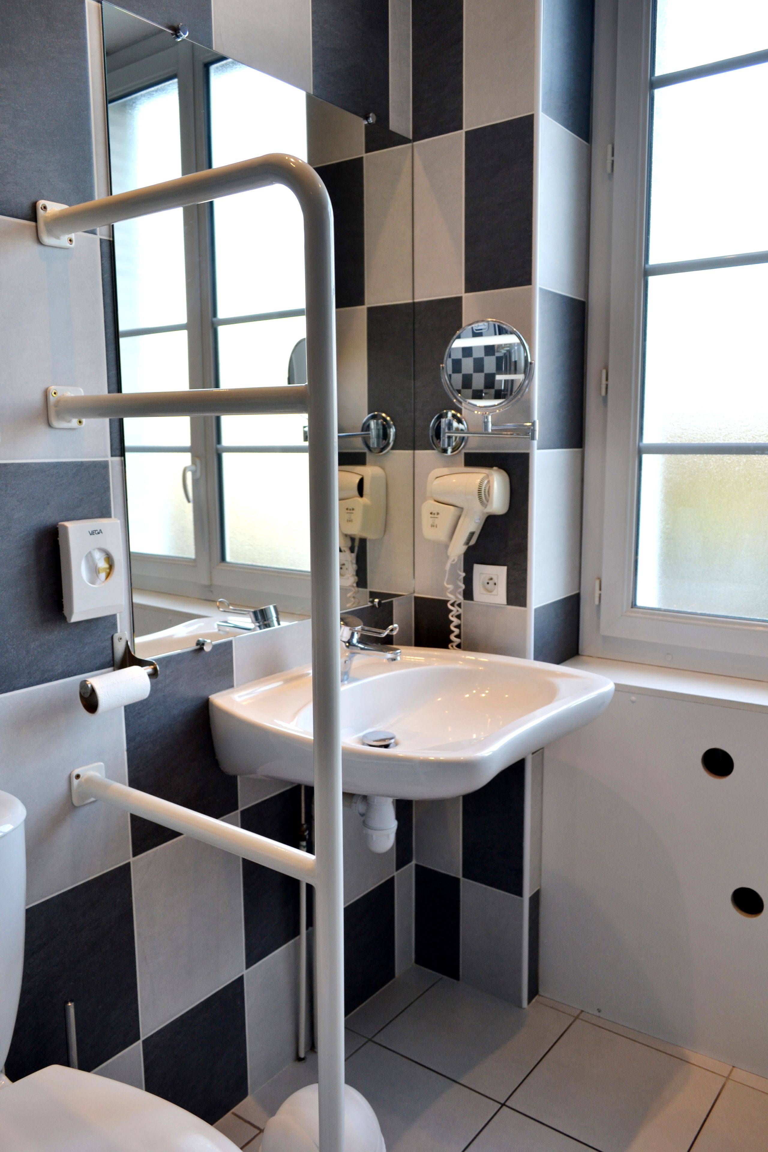 A modern bathroom with a checkered black and white tile wall, a white sink, a mirror, and a hairdryer.