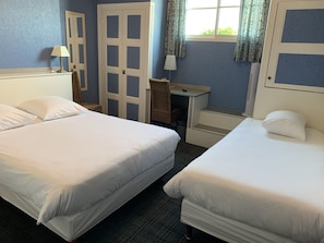 Une chambre d’hôtel avec deux lits, un bureau, une chaise et une fenêtre avec des rideaux.
