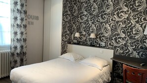 A hotel room with a bed, a desk, and a patterned wallpaper.