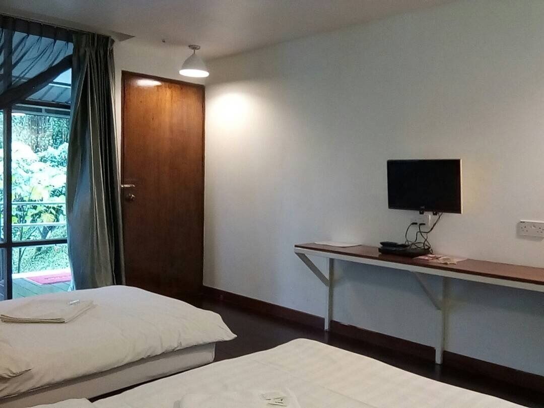 A hotel room with two beds, a desk with a flat-screen TV, a door, and a window with curtains.